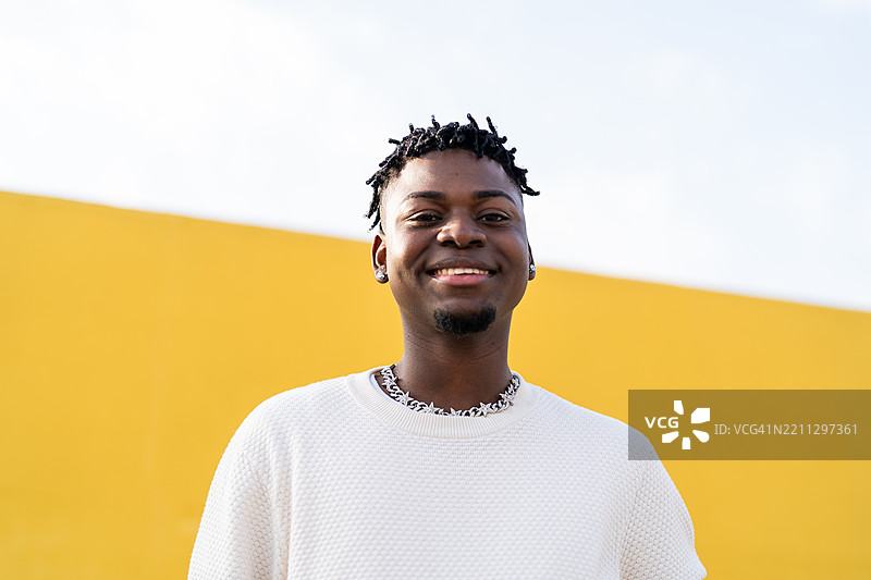 年轻的黑人男子在黄色墙前微笑并摆姿势图片素材