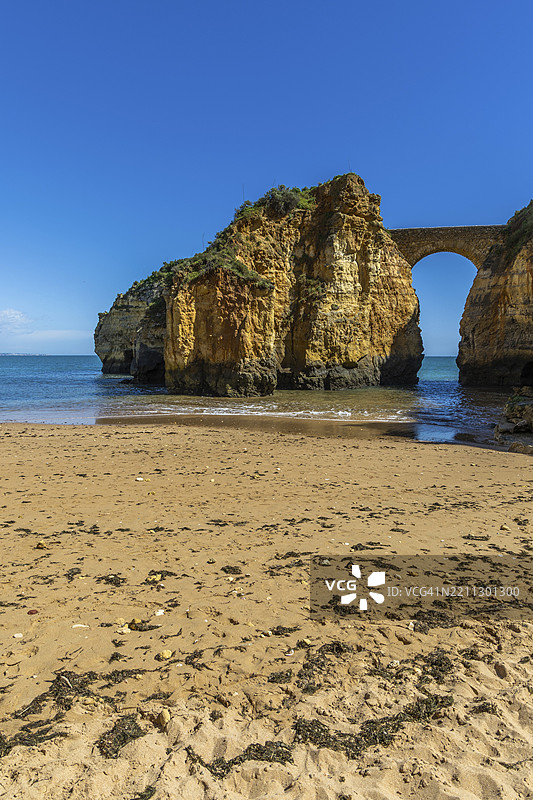 沙滩上的黄色岩石和悬崖。海湾旁,古老的皮尼昂堡石桥连接着两座悬崖。卡尔德拉海滩,拉各斯。阿尔加维,葡萄牙,欧洲图片素材