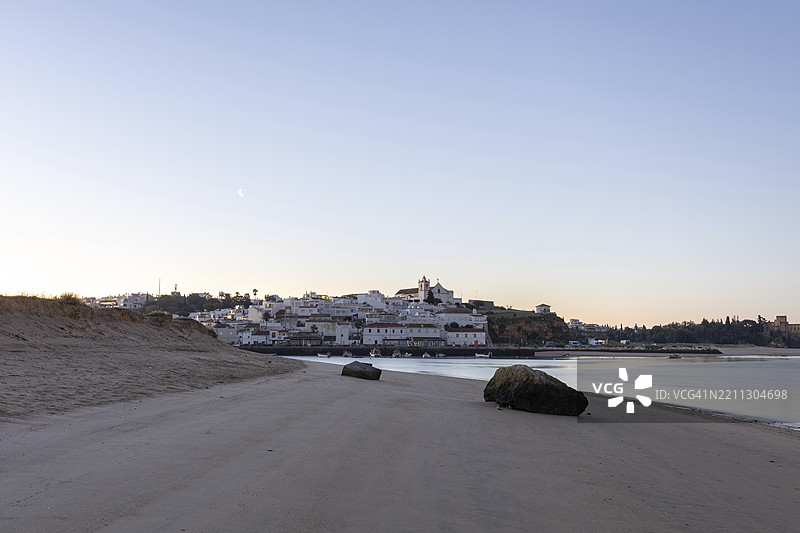 日出时分，低潮下的海滩和港口美景。葡萄牙阿尔加维地区波尔蒂芒费拉古多的历史古镇全景图。图片素材
