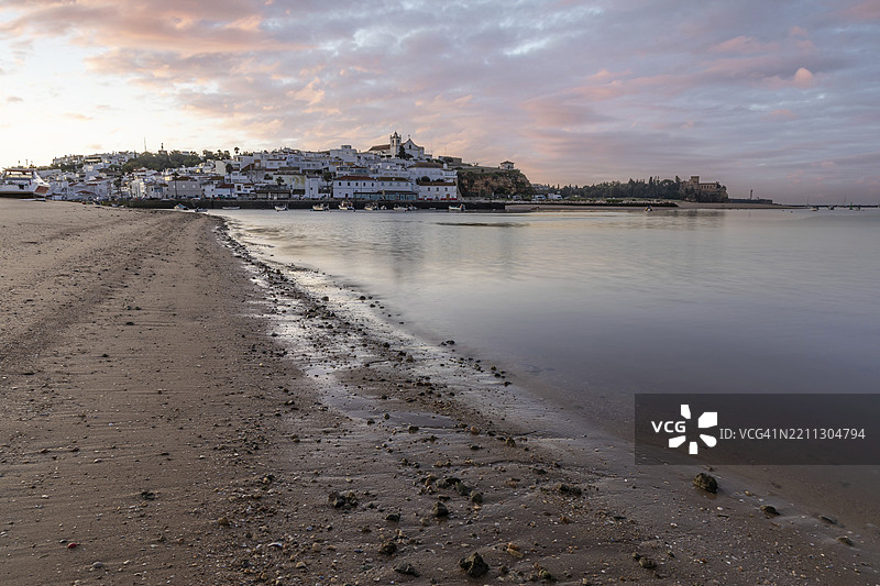 日出时分，低潮下的海滩和港口美景。葡萄牙阿尔加维地区波尔蒂芒费拉古多的历史古镇全景图。图片素材