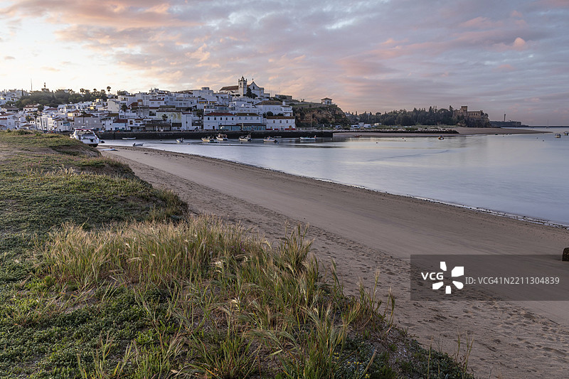 日出时分，俯瞰草地、沙滩和退潮时的港口。葡萄牙阿尔加维地区波尔蒂芒费拉古多的历史古镇全景图。图片素材