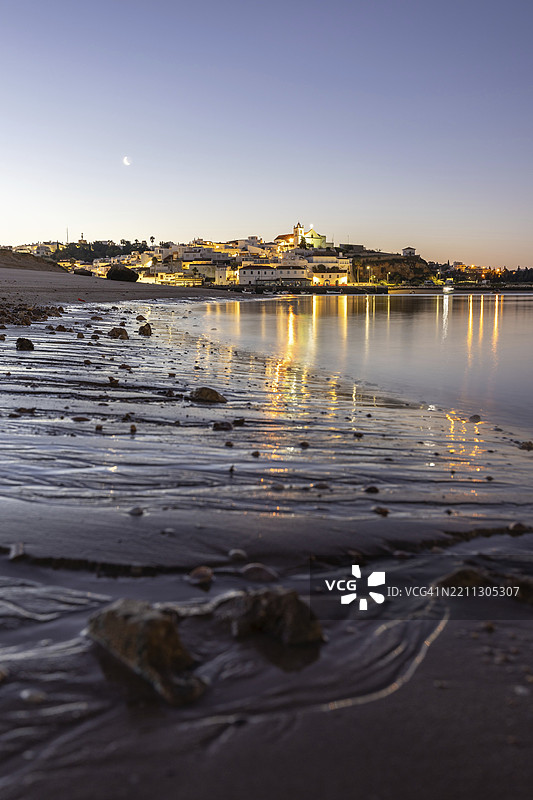 低潮时的沙滩和港口夜景。费拉古多,波尔蒂芒,阿尔加维,葡萄牙,欧洲的黎明时分,照亮的历史市中心全景图。图片素材