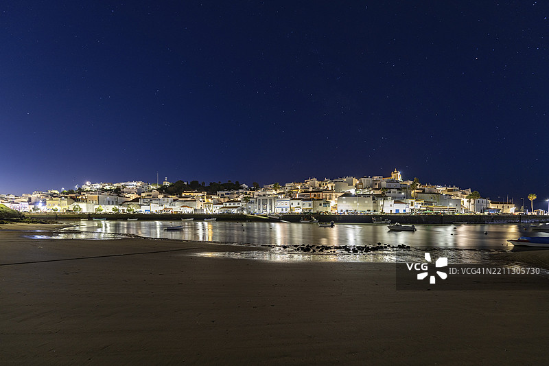 低潮时的沙滩和港口夜景。费拉古多,波尔蒂芒,阿尔加维,葡萄牙,欧洲的黎明时分,照亮的历史市中心全景。图片素材