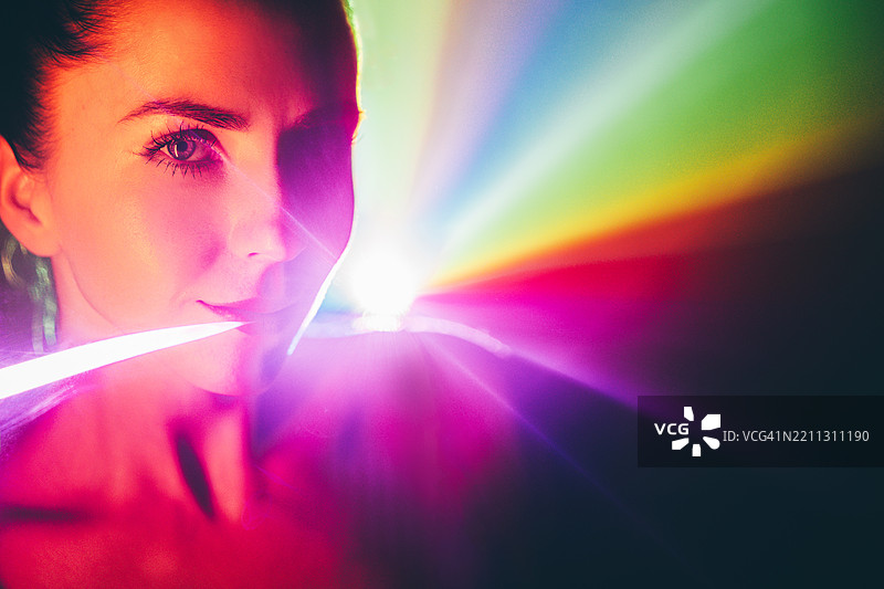 一张女性面部的特写肖像，受到色彩斑斓的光束的戏剧性照明，形成生动的彩虹效果。图片素材