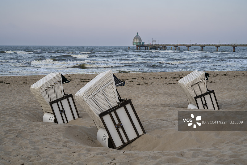 在德国梅克伦堡-前波美拉尼亚州的乌瑟岛齐诺维茨的沙滩上，沙滩椅与潜水舱和码头的景色。图片素材
