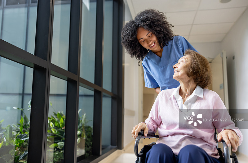 护士微笑着在医院推着一位老年女性的轮椅图片素材
