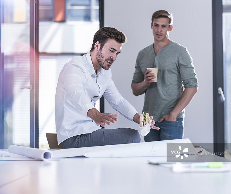 建筑师在办公室里吃三明治，与同事讨论蓝图图片素材