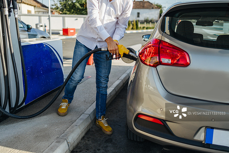 男子在加油站为汽车加油，手握黄色油枪。图片素材