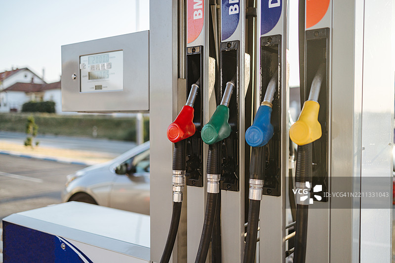 加油站油泵上的油枪悬挂着，背景中有一辆车在等待。图片素材