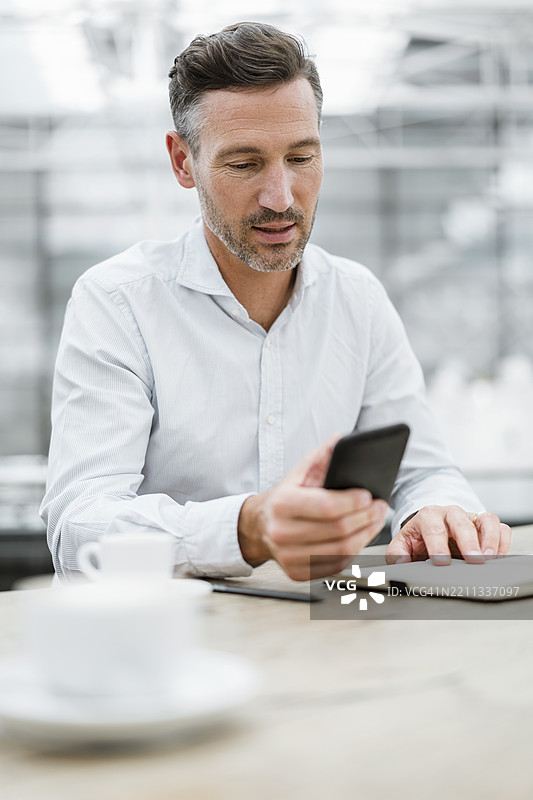 自信的商人在室内使用手机和喝咖啡图片素材