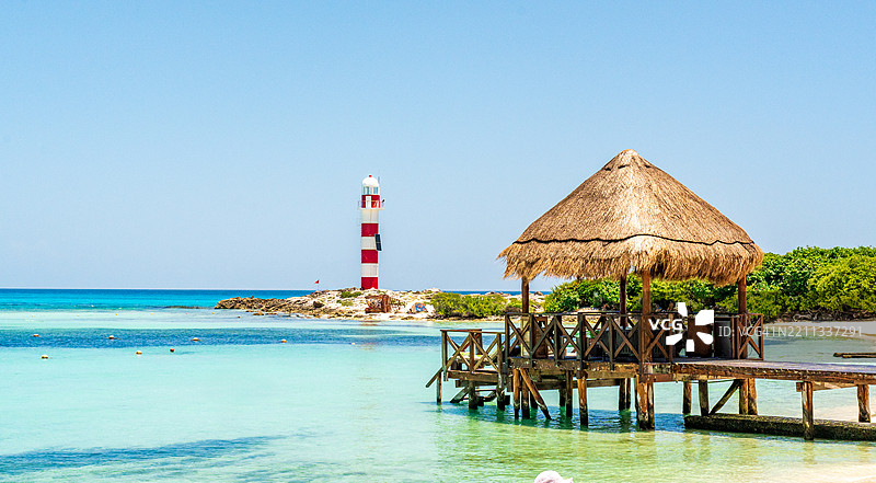 坎昆墨西哥清澈水域中远处的灯塔与茅草屋顶的码头。图片素材