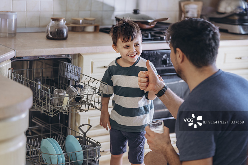 父亲和儿子在厨房一起装载洗碗机图片素材