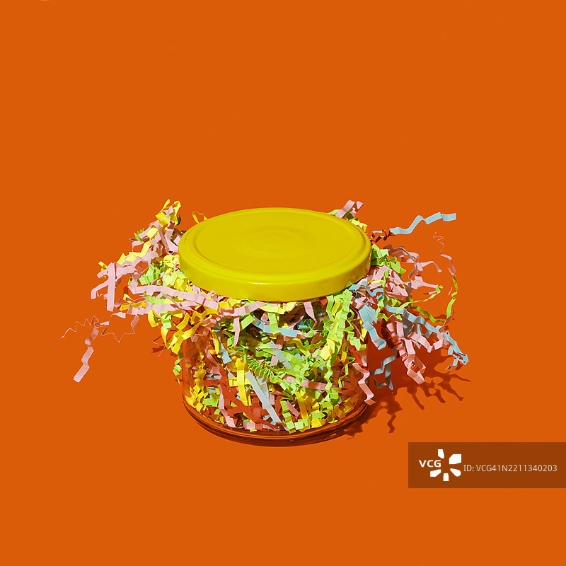 装满五颜六色皱纸条的玻璃罐，背景为橙色图片素材