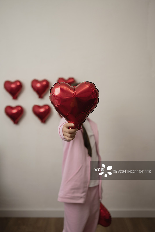 一个女孩在节日的室内环境中拿着一个心形气球图片素材