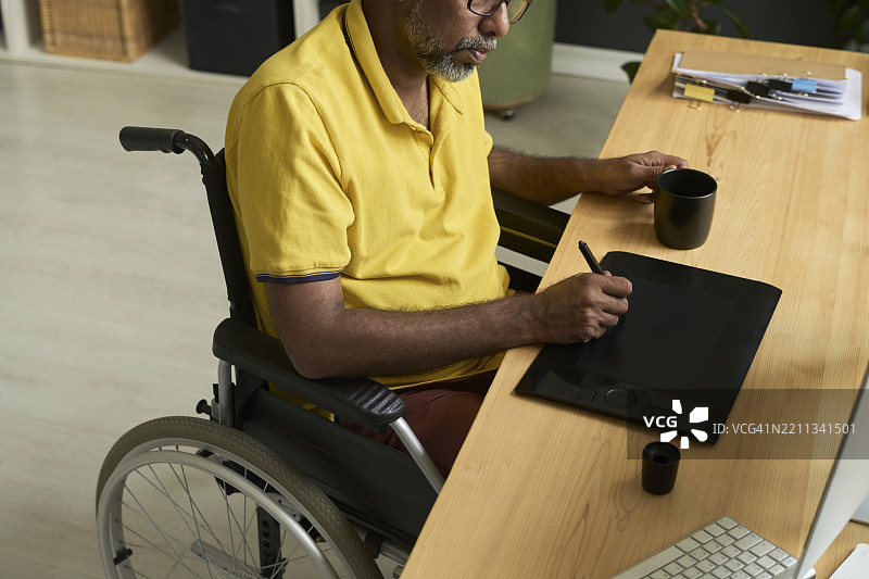 坐在桌子旁的多元文化创作者，使用图形平板电脑。图片素材