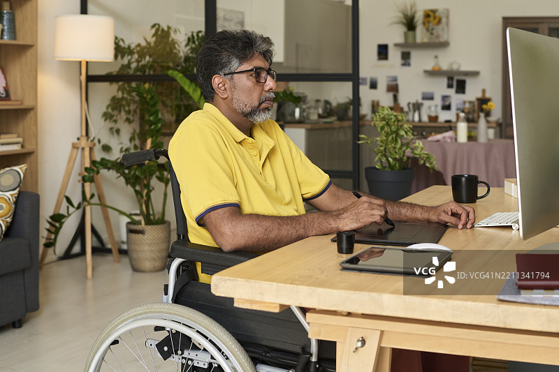坐在轮椅上的严肃平面设计师在家中办公室用平板绘图图片素材