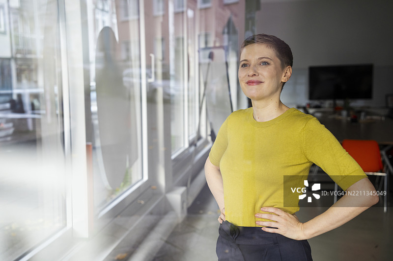 自信的女商人在办公室窗前凝视外面，穿着黄色衬衫。图片素材