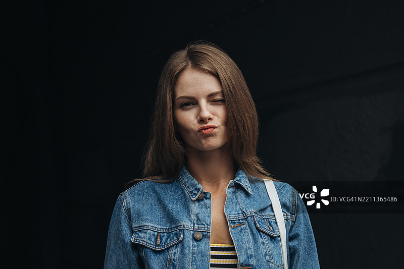 可爱的年轻女性穿着牛仔夹克，在昏暗的环境中撅嘴。图片素材