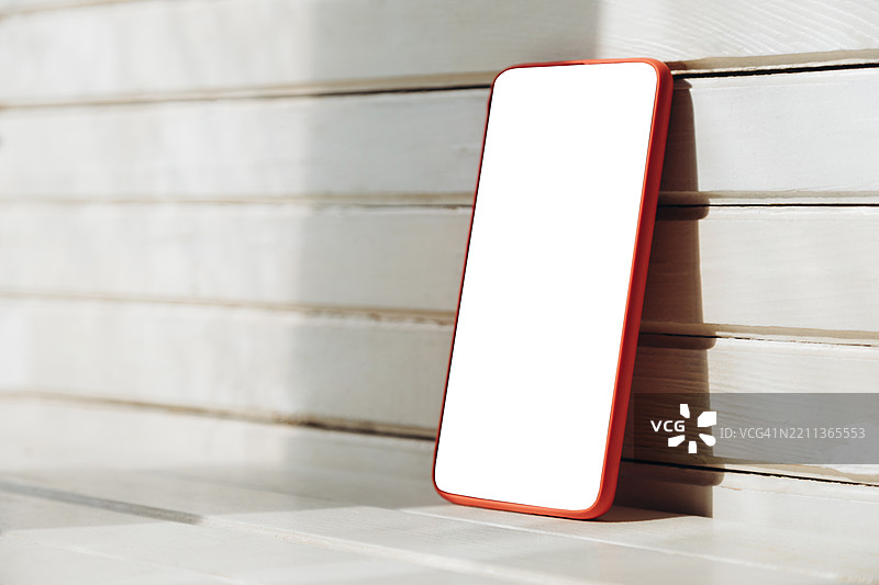 在明亮的木质环境中，白色屏幕的智能手机。图片素材