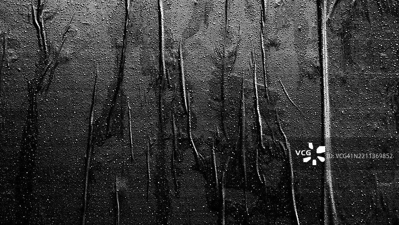 墙上贴着皱褶的黑纸，上面有雨滴。日光与阴影交错。粗糙的纹理。黑白色调。纽约州长岛市（皇后区）。图片素材