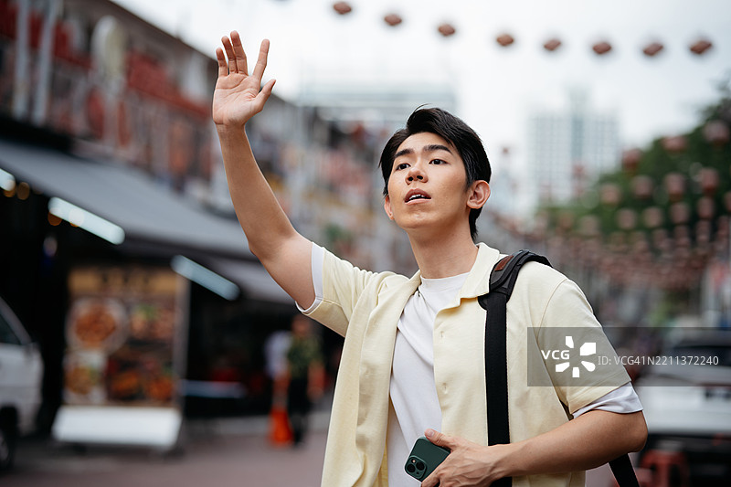 亚洲男子在购物区招手叫网约车图片素材