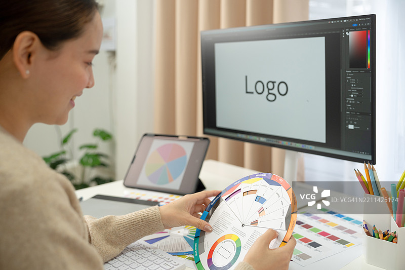 年轻的亚洲女性平面设计师在记录标志设计的笔记。平面设计师在笔记本电脑上工作，并使用图形绘图笔。图片素材