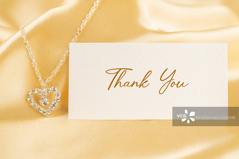 感谢卡和镶有钻石的银项链，背景为金色丝绸。图片素材