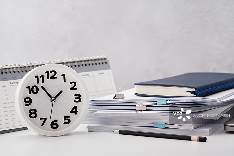 白色桌子上堆放着一堆文件和纸张，旁边有一个闹钟。截止日期图片素材