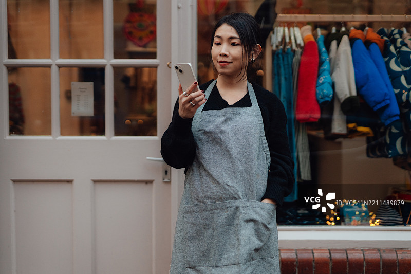 女性小企业主在店门口使用智能手机图片素材