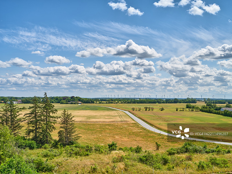 宁静的春季风景，郁郁葱葱的草地，蜿蜒的道路，以及远处在明亮天空下的风力发电机阵列图片素材