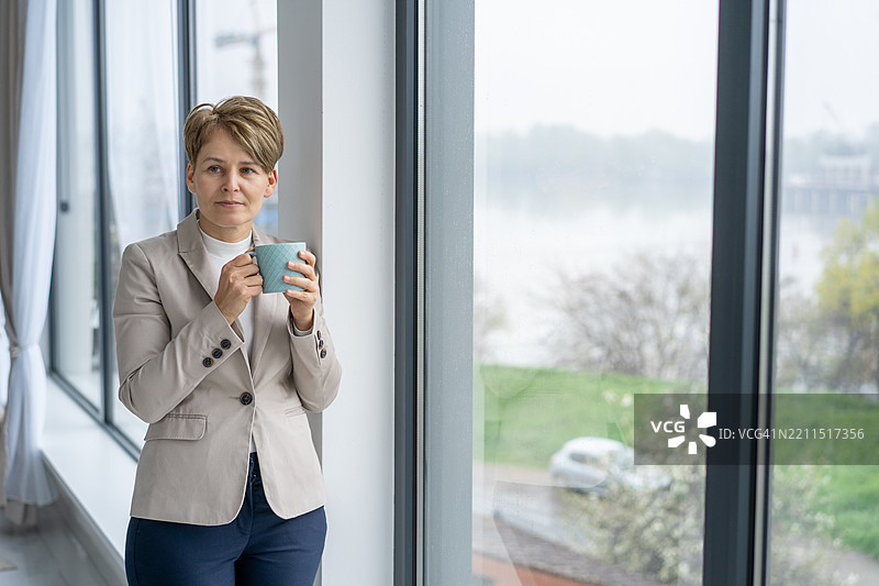 女人手握杯子，若有所思地望向窗外图片素材