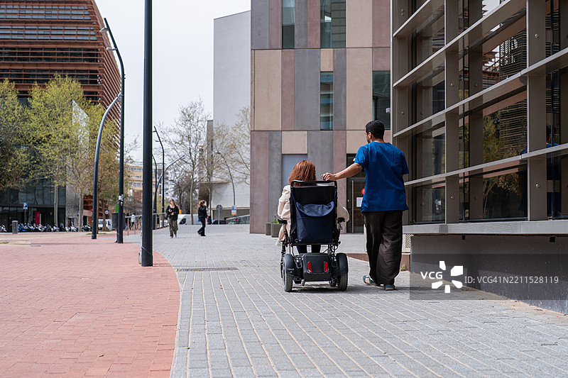 护士在城市人行道上推着坐在轮椅上的病人图片素材