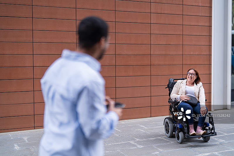 微笑的女商人在户外用轮椅向同事打招呼图片素材