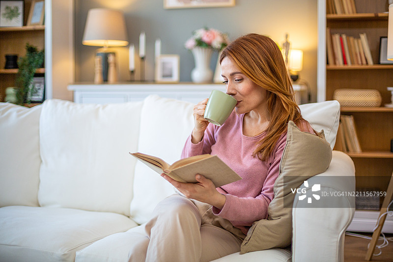 女人在沙发上放松，阅读一本书并喝茶图片素材