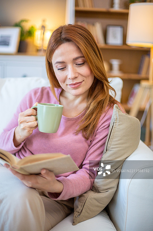 女人在沙发上放松，阅读书籍并喝茶图片素材