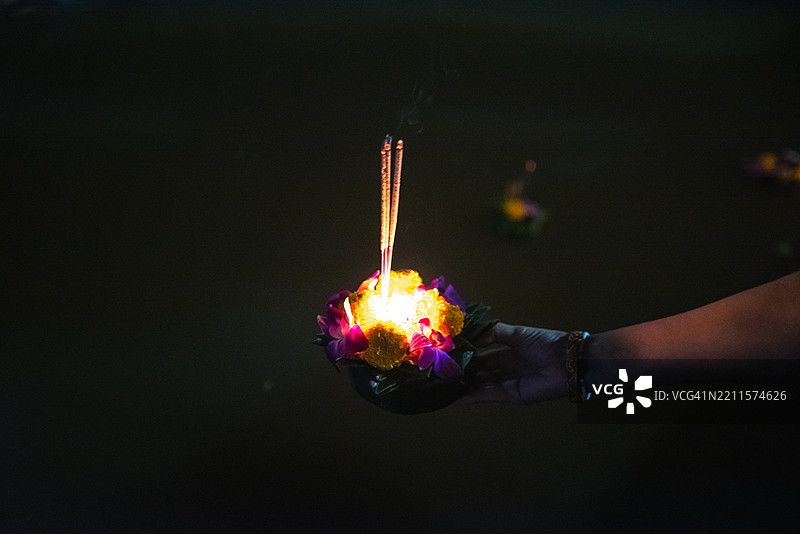 在泰国水灯节上，一个无法辨认的女性正在河中投放祭品。图片素材