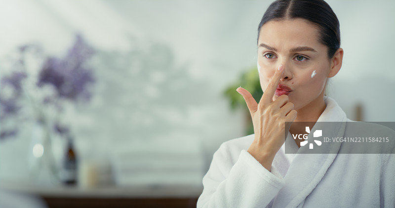 在浴室里涂抹护肤乳液的女性，进行美容和皮肤护理，关注健康。一个顽皮的女孩在镜子前化妆，使用化妆品进行护肤和清洁。图片素材