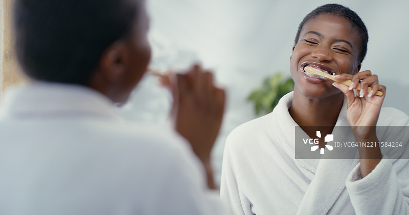 黑人女性在浴室用牙刷刷牙，进行口腔护理或口腔卫生。女性在家中镜子前，使用竹棒清洁口腔和牙龈，进行早晨日常护理。图片素材