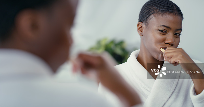 黑人女性在浴室里对着镜子刷牙，进行口腔护理或牙齿卫生。女性，嘴巴和早晨例行公事的倒影，保持清新口气或牙龈健康。图片素材