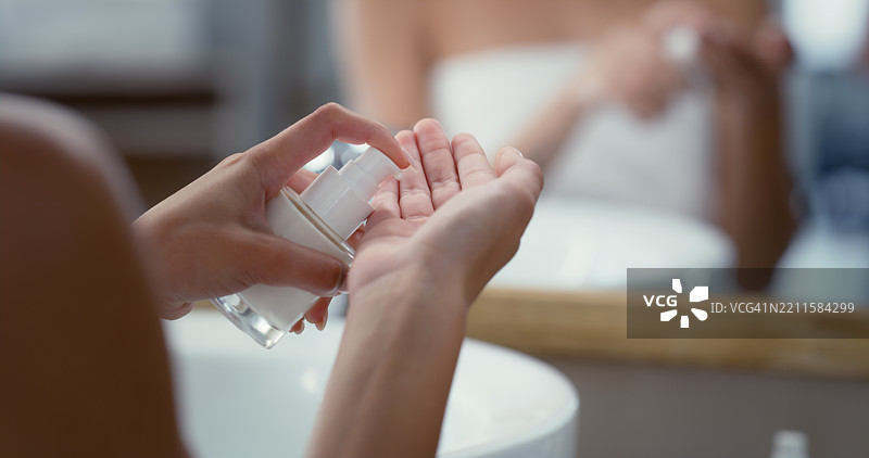 浴室里的人，手中拿着护肤乳液或分配器，早晨护肤程序或家用化妆品。特写镜头，容器和镜子中有用于皮肤护理的产品精华、油或保湿霜。图片素材