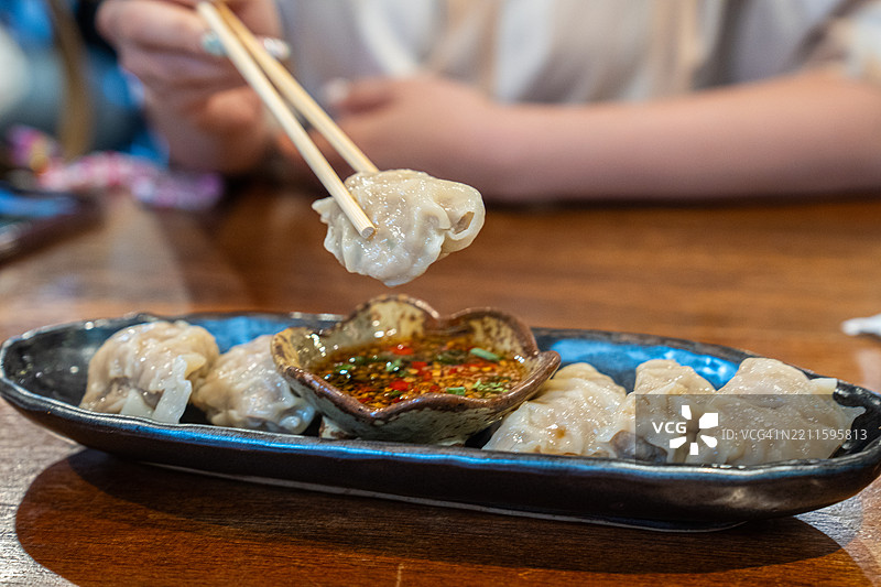 这张裁剪的图片展示了一位年轻的亚洲女性在餐厅里吃蒸饺。图片素材