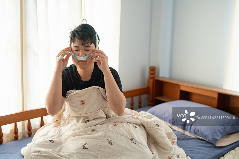 一名患有阻塞性睡眠呼吸暂停症（OSA）的男子，身上缠绕着管子，并使用CPAP呼吸机。图片素材