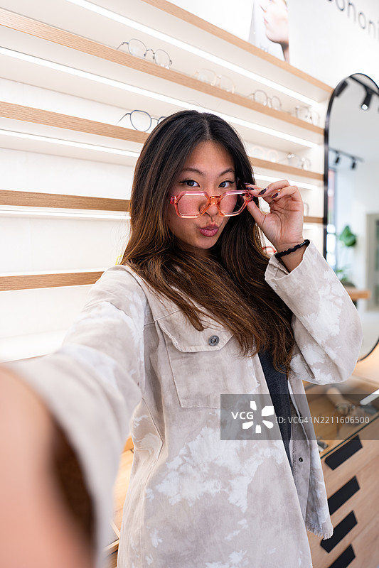 年轻女性在眼镜店试戴时尚眼镜并自拍图片素材