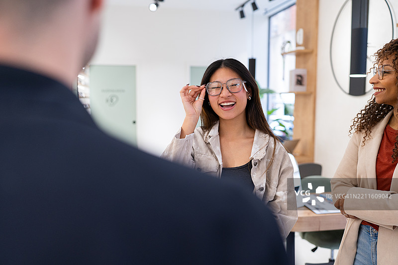 年轻女性在眼镜店与朋友一起试戴新眼镜图片素材