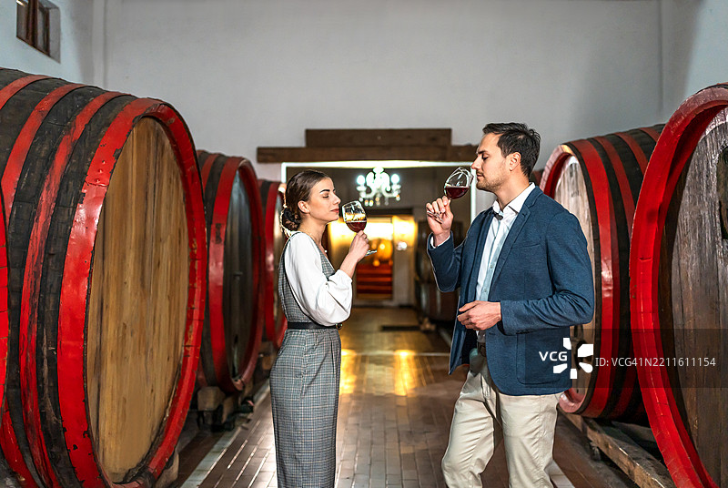年轻男女在酒窖中闻酒，周围是橡木桶图片素材