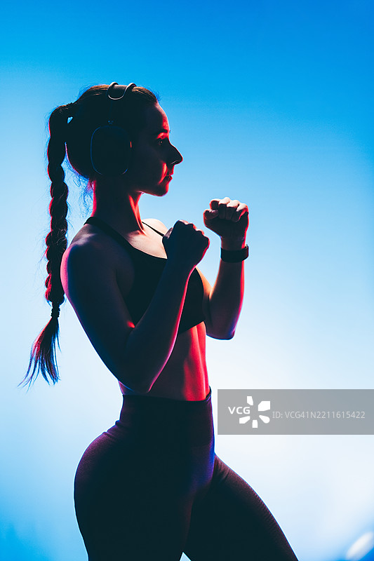 自信的年轻白人女性在霓虹灯下进行影子拳击。图片素材