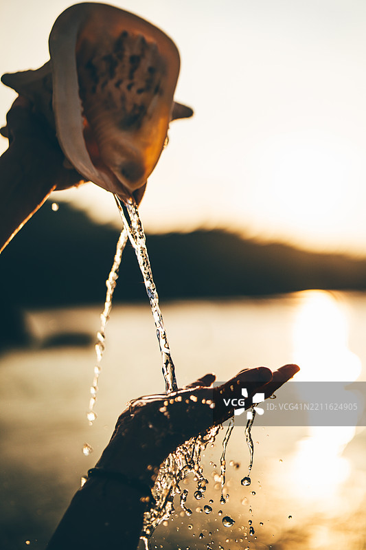 女人用海螺倒水，手部特写。图片素材