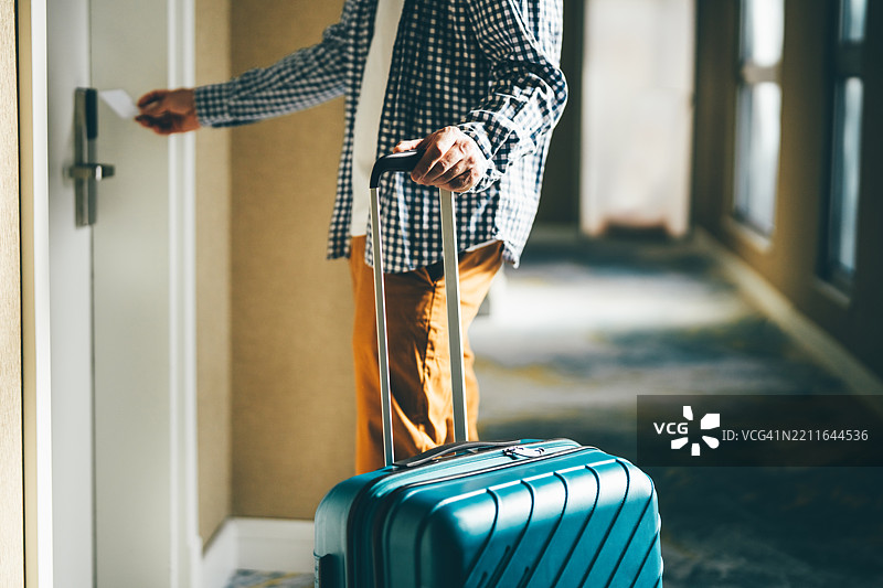 男子使用房卡打开酒店房门，手里拿着一个浅蓝色的行李箱。图片素材