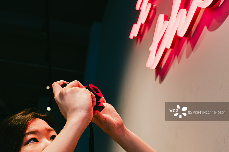 年轻女性摄影师用复古相机拍摄霓虹灯标志图片素材