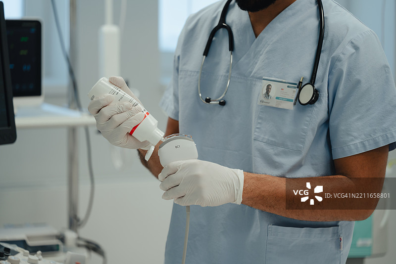 医生在腹部扫描前将超声波凝胶涂抹在探头上图片素材